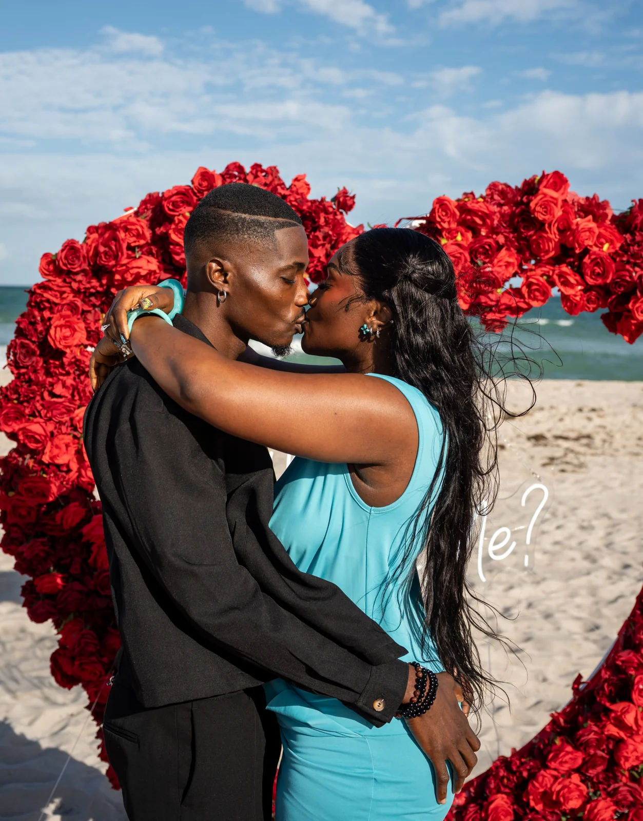 The newly engaged couple kisses on the beach.